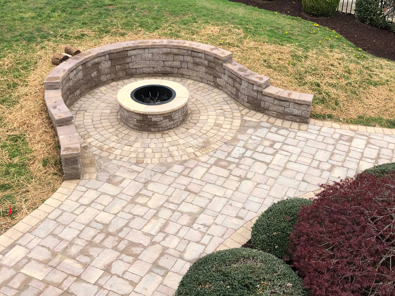 Paver patio with graduated seating wall and permanent firepit with capstone and metal insert. 