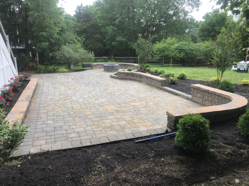 paver patio with footer wall.  Raised bed.  Seating wall with capstone.  Landsaping. Wallstone firepit with metal insert. 